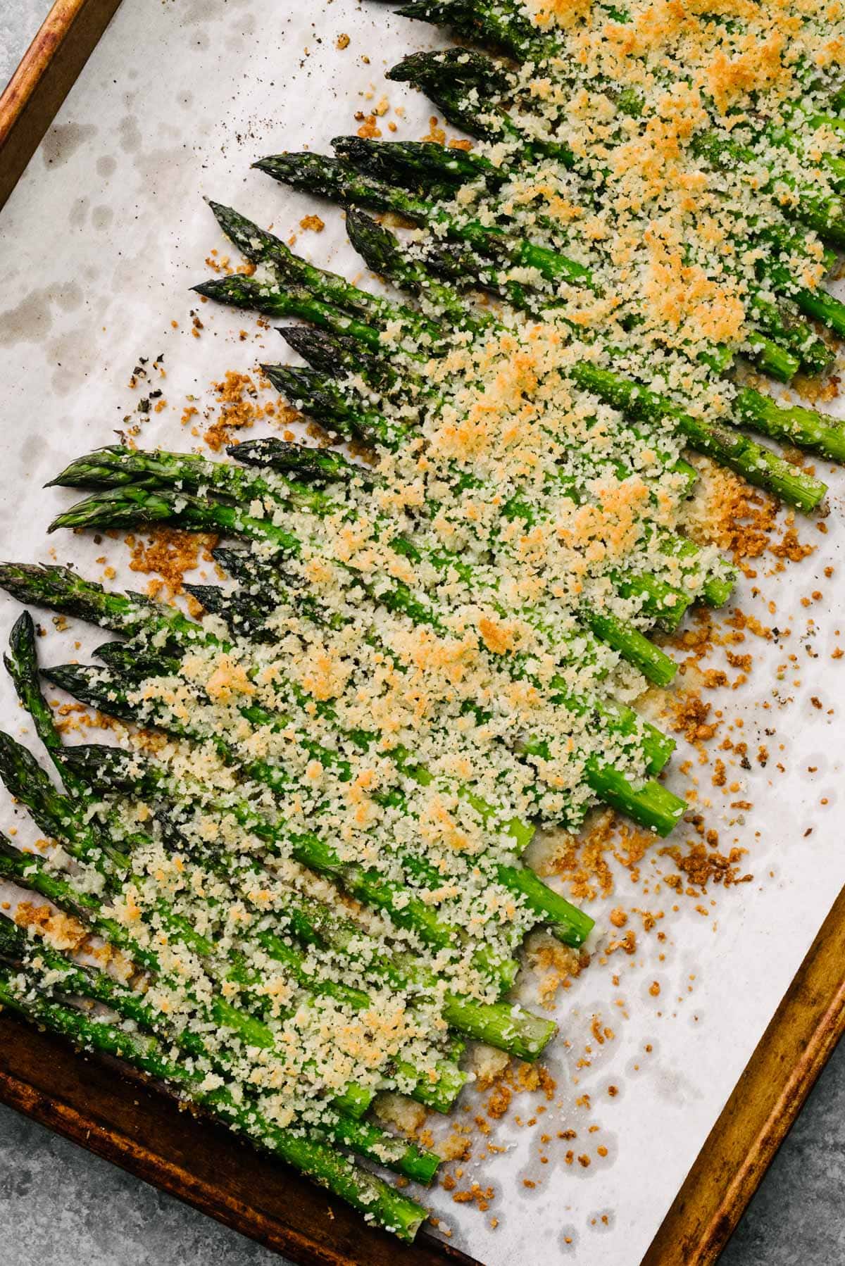 Roasted asparagus spears topped with a crispy parmesan and panko breadcrumb topping on a parchment lined baking sheet.