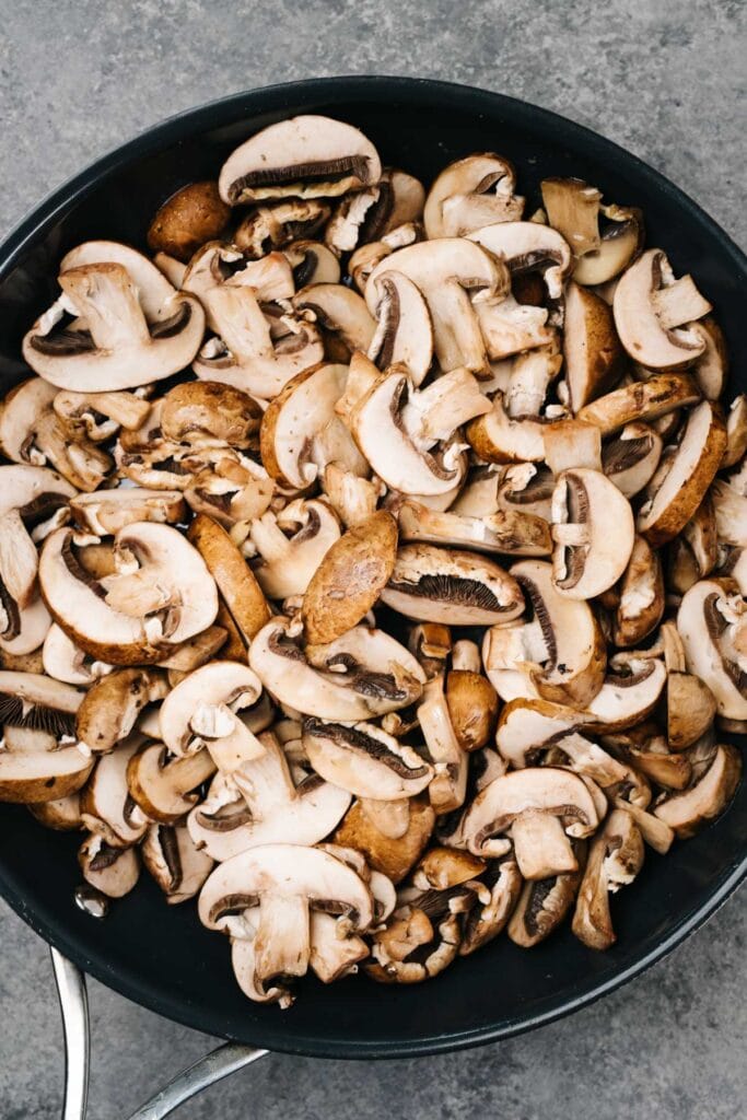 Sliced mushrooms tossed with olive oil and butter in a skillet, but still raw.