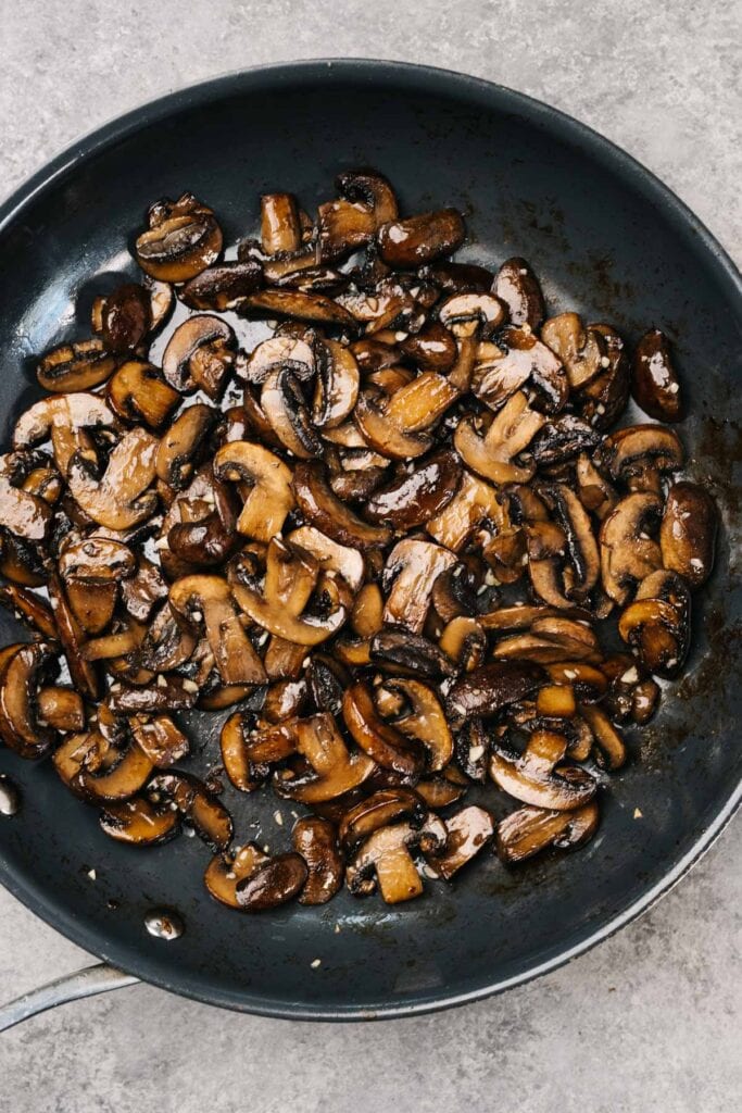 Crispy, golden brown sauteed mushrooms in a skillet on a concrete background.