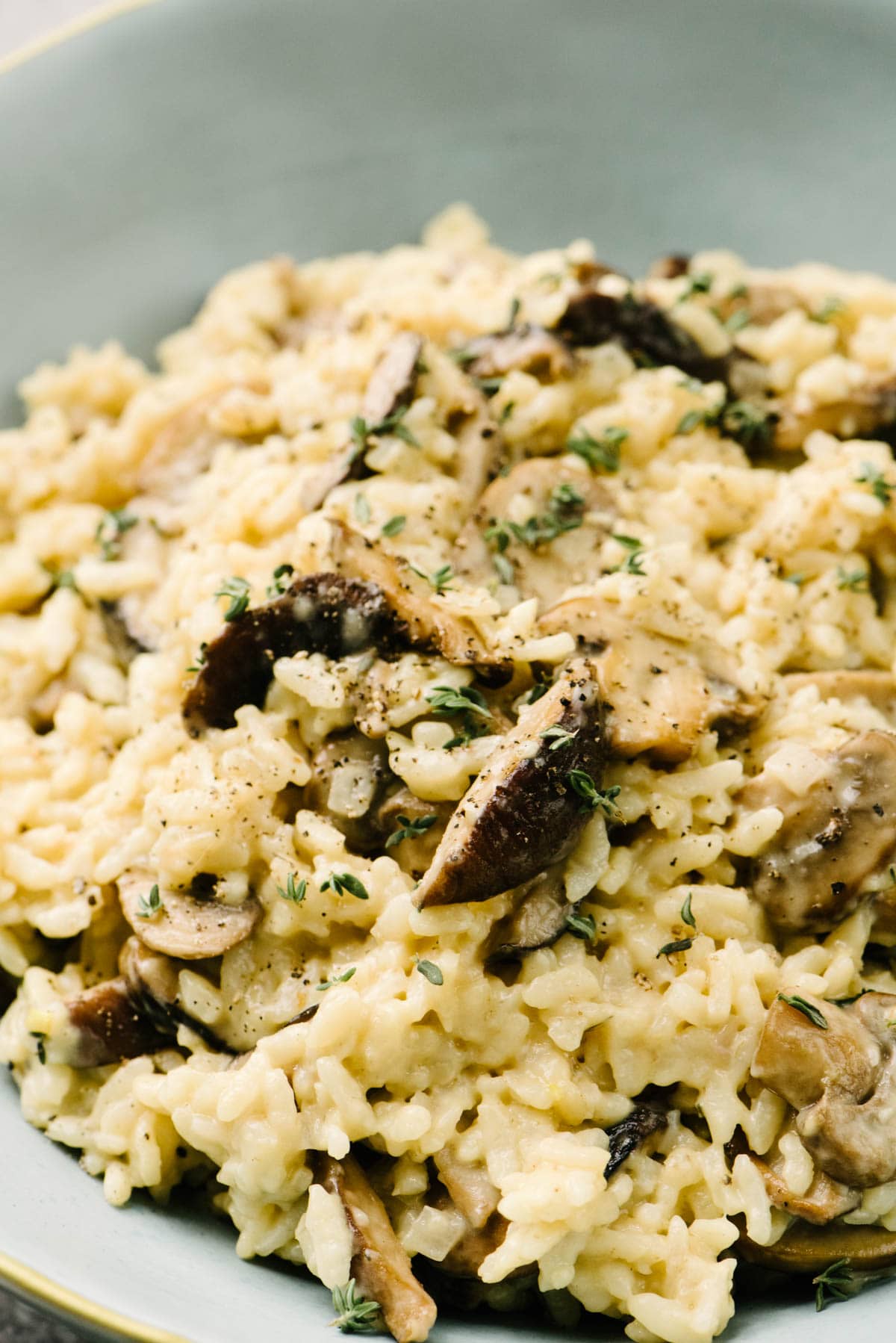 Side view, creamy mushroom risotto in a light blue serving bowl, garnished with fresh thyme leaves.
