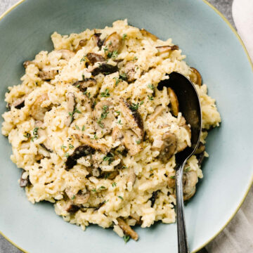 Instant Pot mushroom risotto in a blue serving bowl with a silver serving spoon, garnished with fresh thyme.