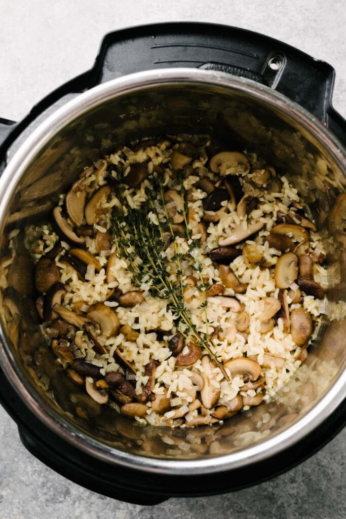Cooked mushroom risotto in an Instant Pot topped with a thyme stem.
