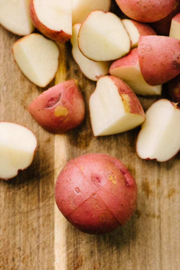 Quartered red baby potatoes on a cutting board with one potato showing the cut lines for making bite-sized pieces.