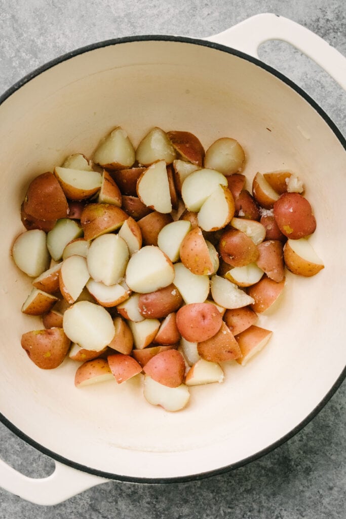 Cooked baby red potatoes in a large white dutch oven.