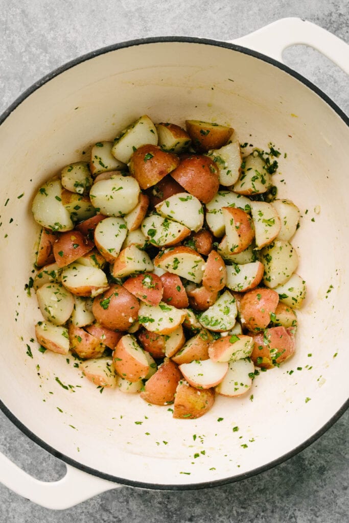 Boiled red potatoes tossed with herb vinaigrette in a large white dutch oven.