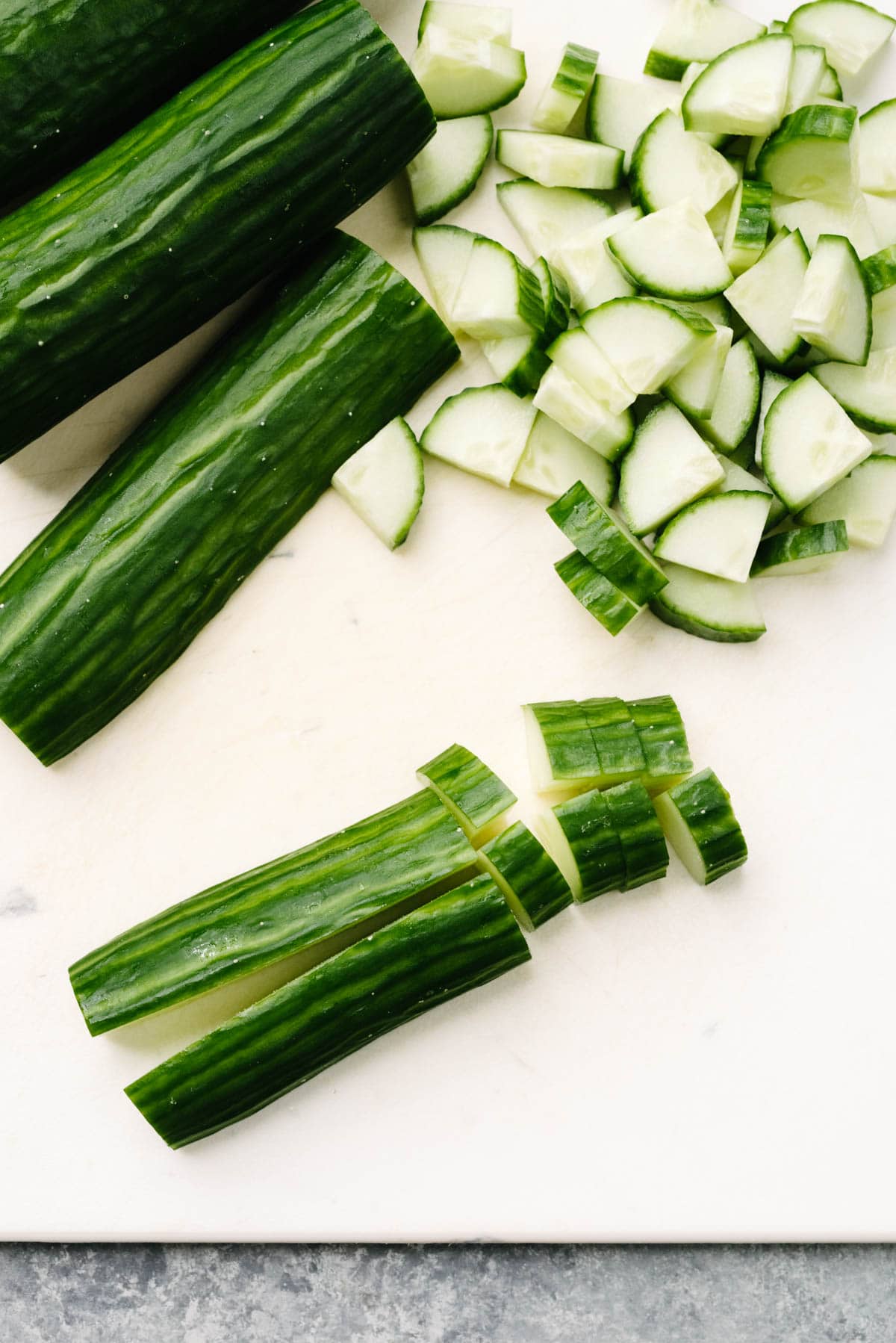 English cucumbers divided into quarters and then thinly sliced on a white cutting board.