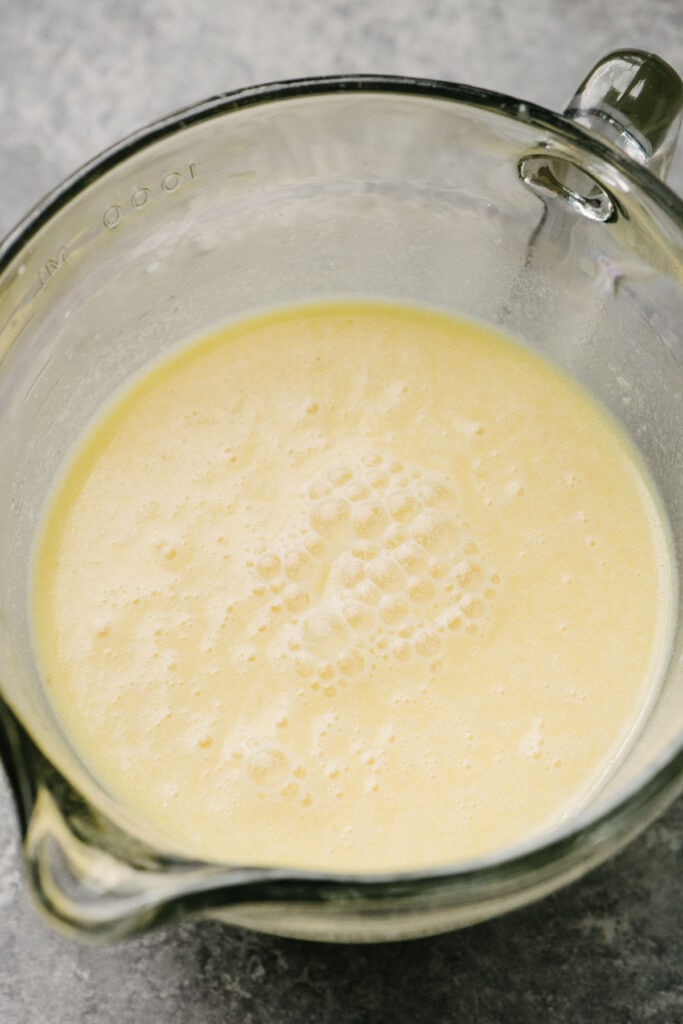 Side view, milk, eggs, vanilla extract, and melted butter whisked until very smooth in 4-cup measuring cup.