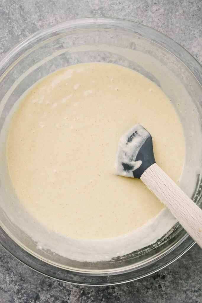 Pancake batter gently folded together in a large glass mixing bowl with a rubber spatula.
