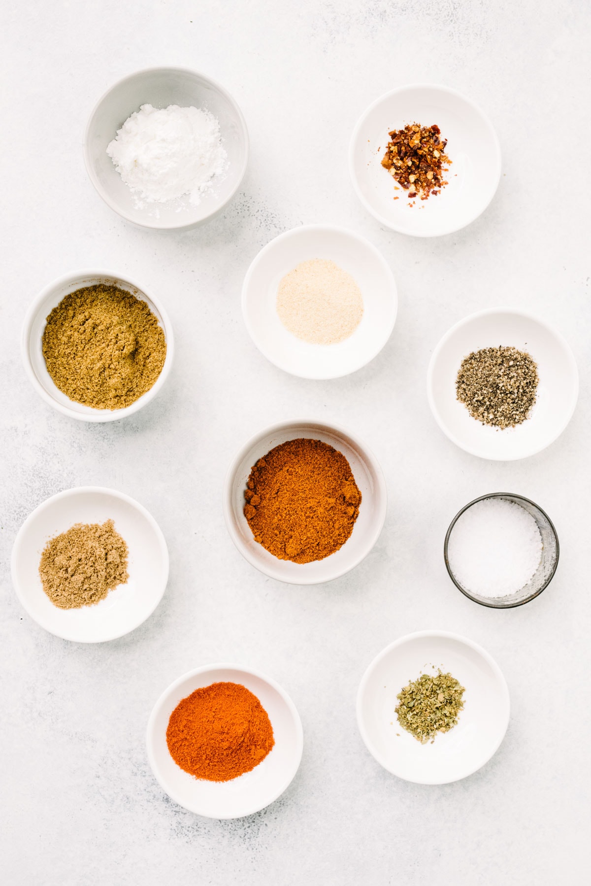 The ingredients for homemade ground beef taco seasoning in small bowls arranged on a concrete background.