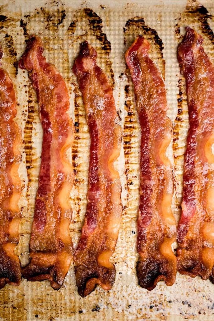 Cooked bacon with some crispy bits and some soft bits on a parchment lined baking sheet.
