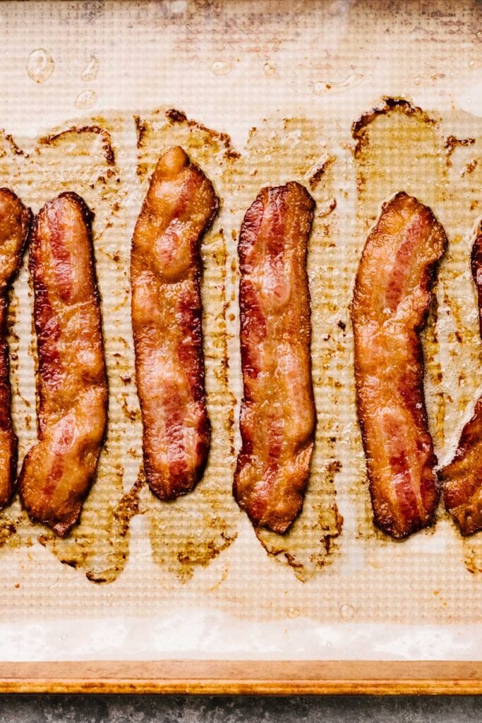Evenly cooked strips of bacon on a parchment lined baking sheet.