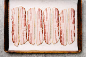 Eight slices of bacon arranged in a single, even layer on a parchment lined baking sheet.