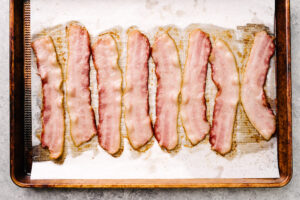 Partially cooked strips of bacon on a parchment lined baking sheet.