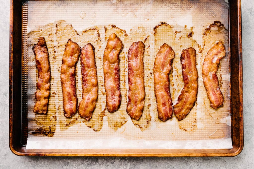 Crispy slices of cooked bacon on a parchment lined baking sheet.
