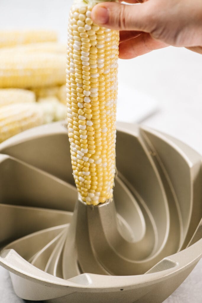 Side view, a hand holding a corn cob in the center of a bundt pan.