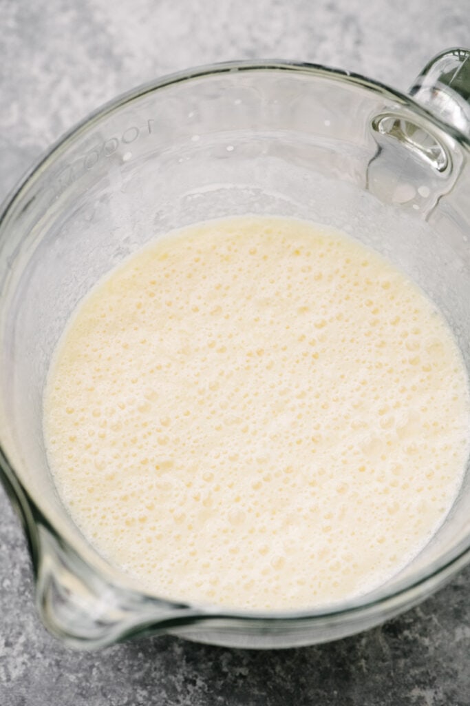 Side view, melted butter, egg, milk, and vanilla whisked until frothy in a large glass mixing cup.