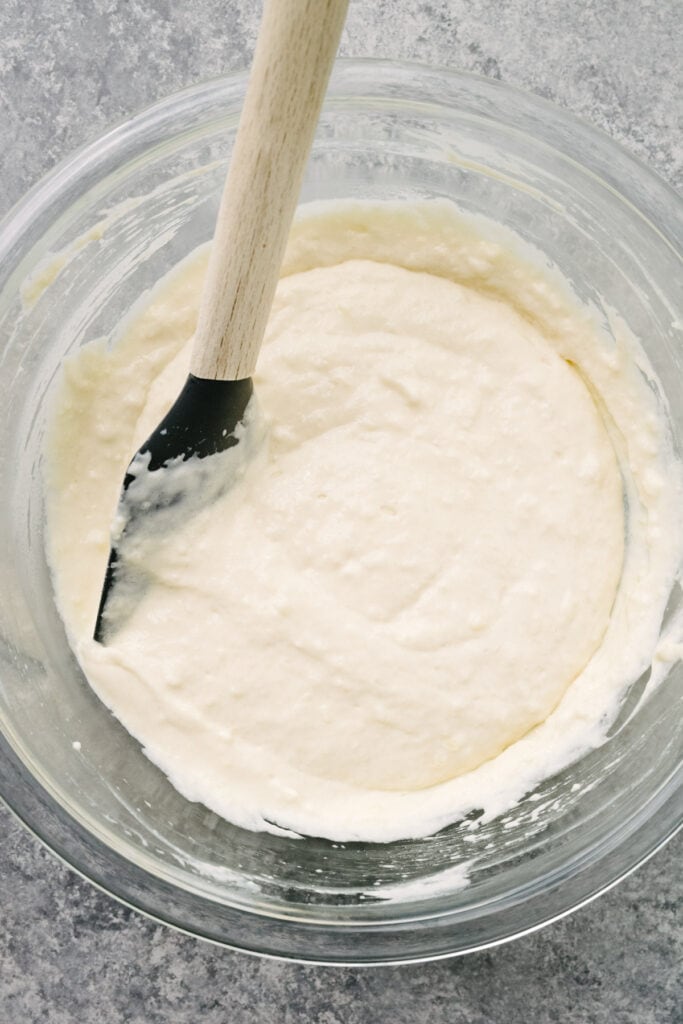 Homemade pancake batter resting in a large glass mixing bowl with a rubber spatula tucked into the batter.