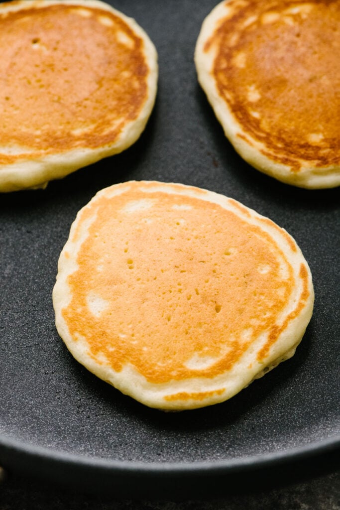 Side view, three golden brown cooked pancakes in a non-stick skillet.