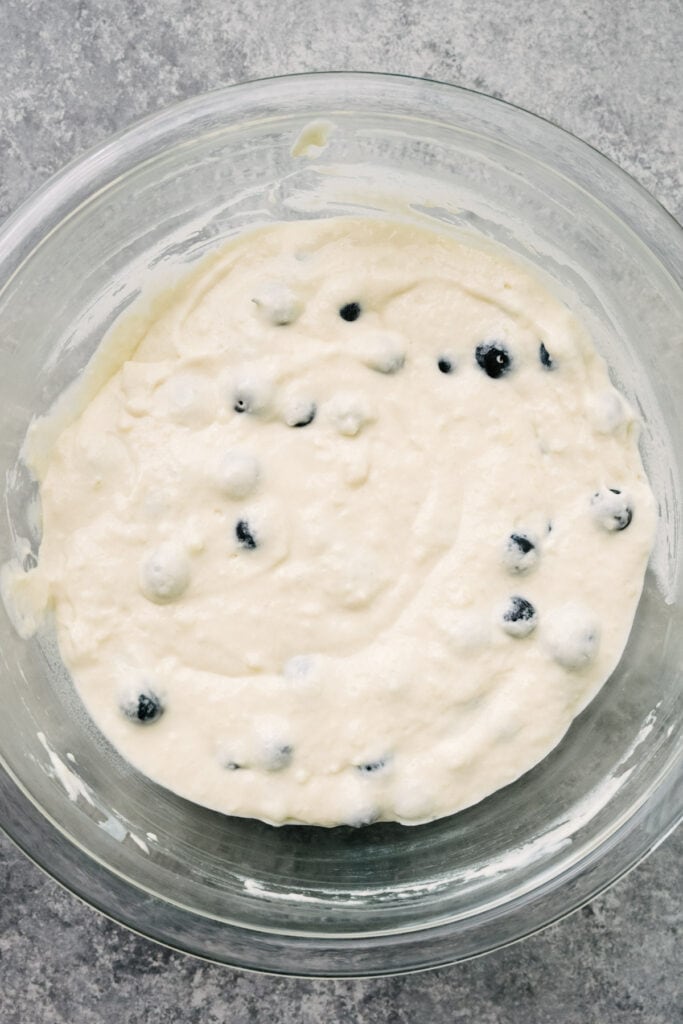 Homemade blueberry buttermilk pancake batter resting in a large glass mixing bowl.