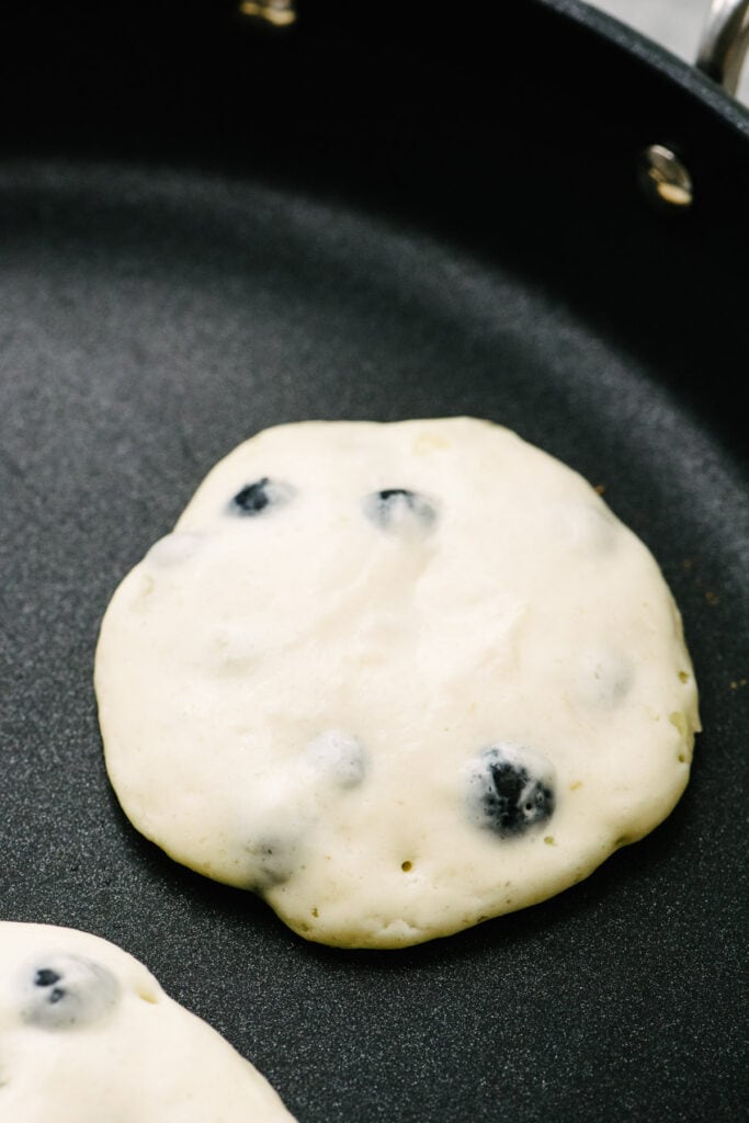 Side view, blueberry buttermilk pancakes cooking in a skillet showing bubbles on the surface of the pancakes and firm edges.