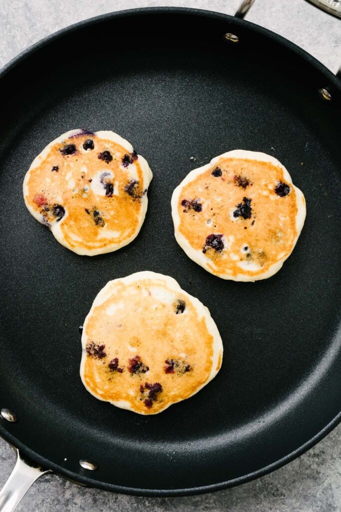 Three cooked blueberry buttermilk pancakes in a large non-stick skillet.