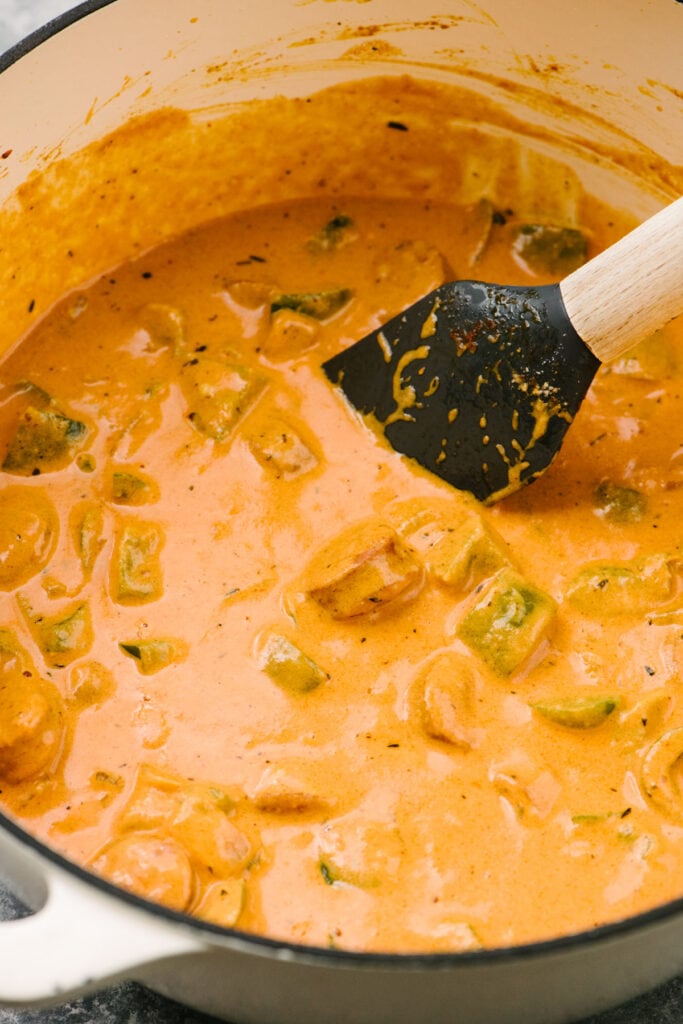 Side view, a rubber spatula tucked into a pot filled with creamy cajun pasta sauce before adding pasta.