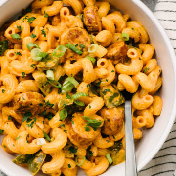 A fork tucked into a bowl of creamy cajun sausage pasta, garnished with green onions.