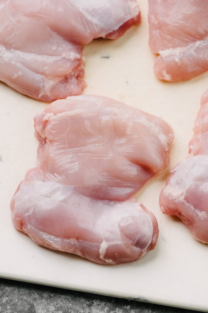 Side view, boneless skinless chicken thighs with visible fat trimmed away on a cutting board.