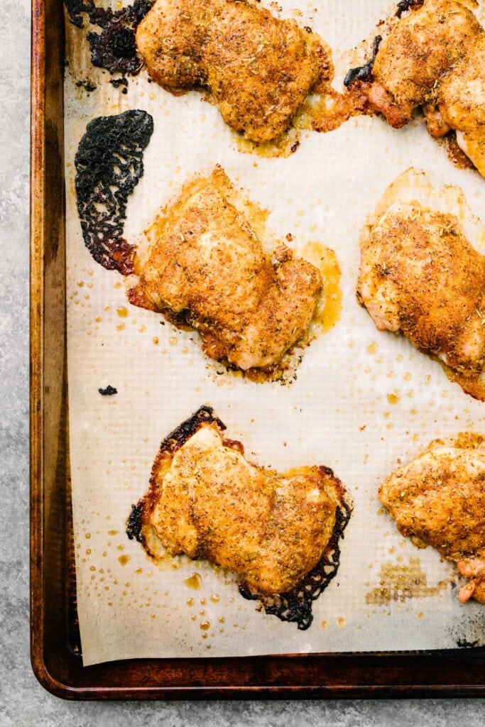 Crispy baked boneless skinless chicken thighs on a parchment lined baking sheet.