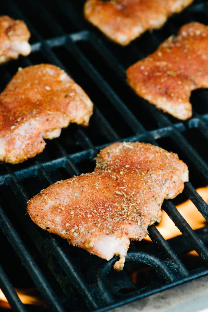 Side view, raw chicken thighs on the grates of a grill, cooking over high heat.