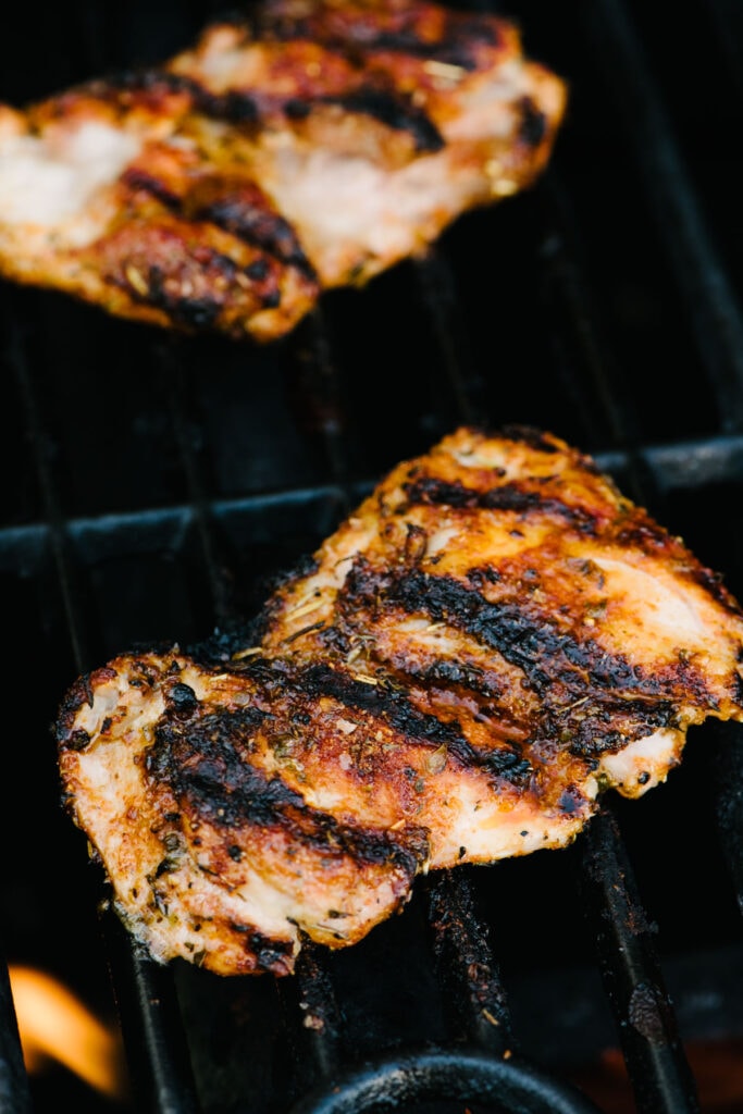 Side view, boneless chicken thighs with visible char marks on a hot grill.