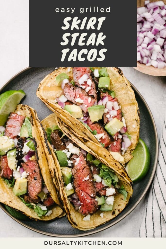 Three skirt steak tacos in corn tortilla shells on a grey plate, each topped with diced avocado, red onion, and crumbled queso fresco cheese; title bar at the top reads "easy grilled skirt steak tacos"