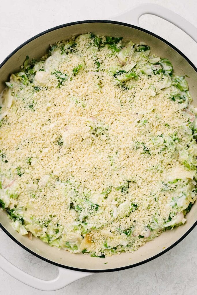 Brussels sprouts au gratin topped with bread crumbs in a large grey skillet before baking in the oven.