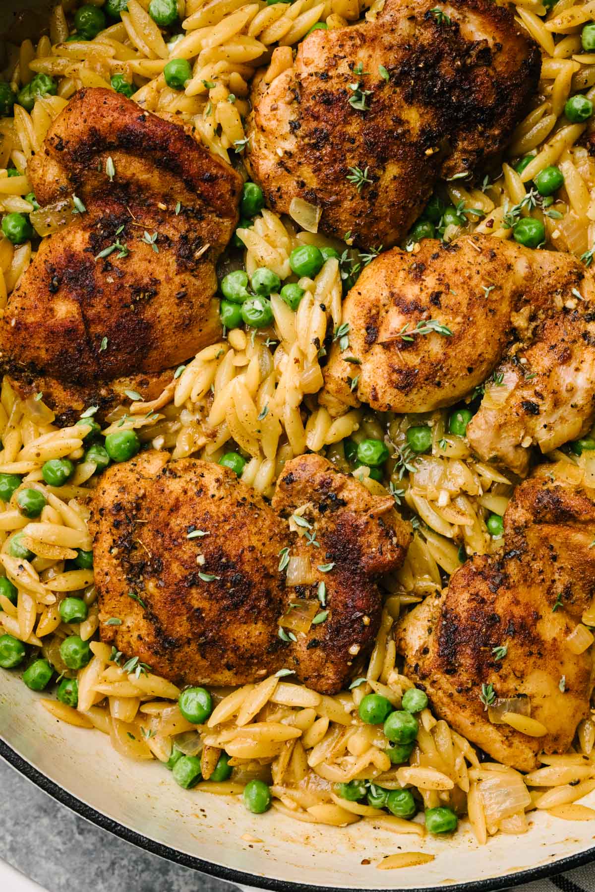 Seared chicken thighs nestled into a skillet of cooked orzo pasta with peas, parmesan cheese, and fresh thyme.