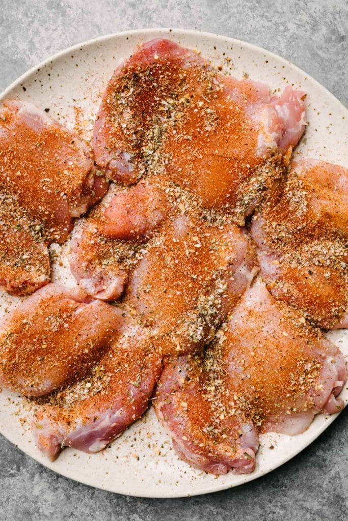 Boneless skinless chicken thighs on a plate seasoned with Italian seasoning, paprika, garlic powder, onion powder, salt, and pepper.