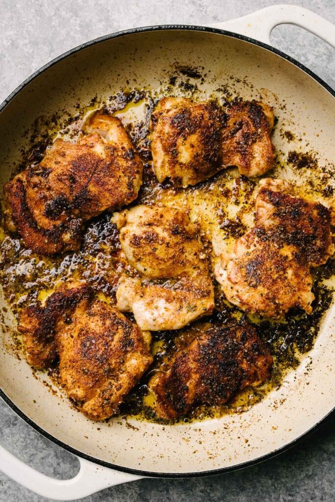 Seared boneless chicken thighs in a large grey enameled skillet.