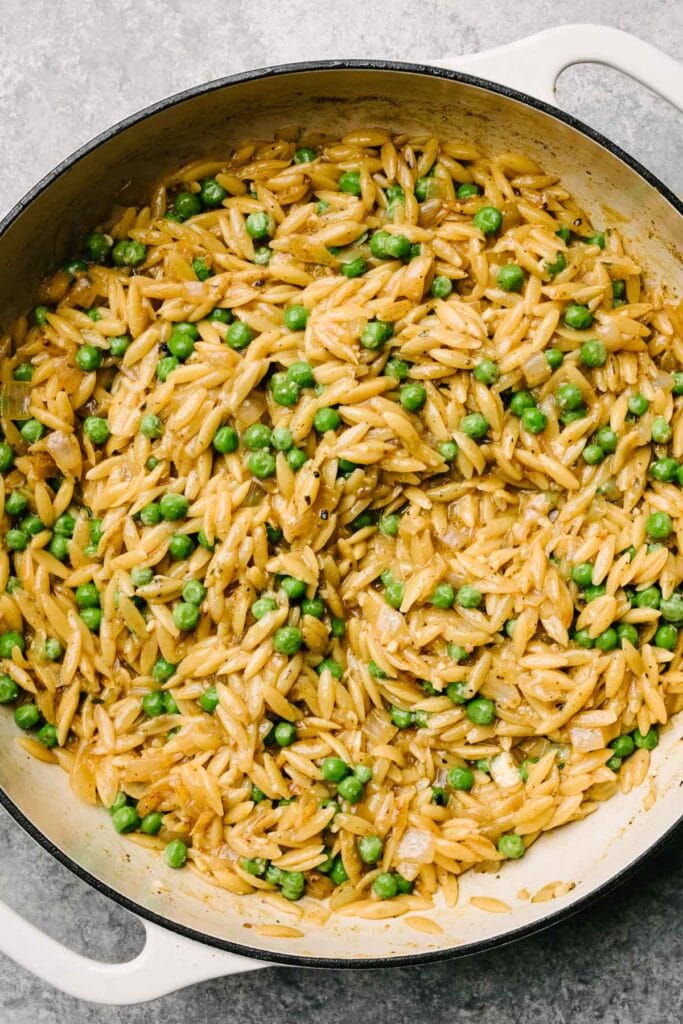 Creamy orzo pasta with peas and parmesan cheese in a large grey enameled skillet.