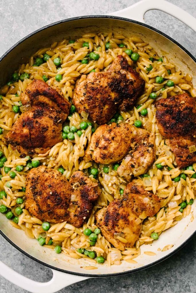 One pot chicken and orzo skillet with seared boneless chicken thighs over orzo pasta with peas and parmesan in a large grey enameled skillet.