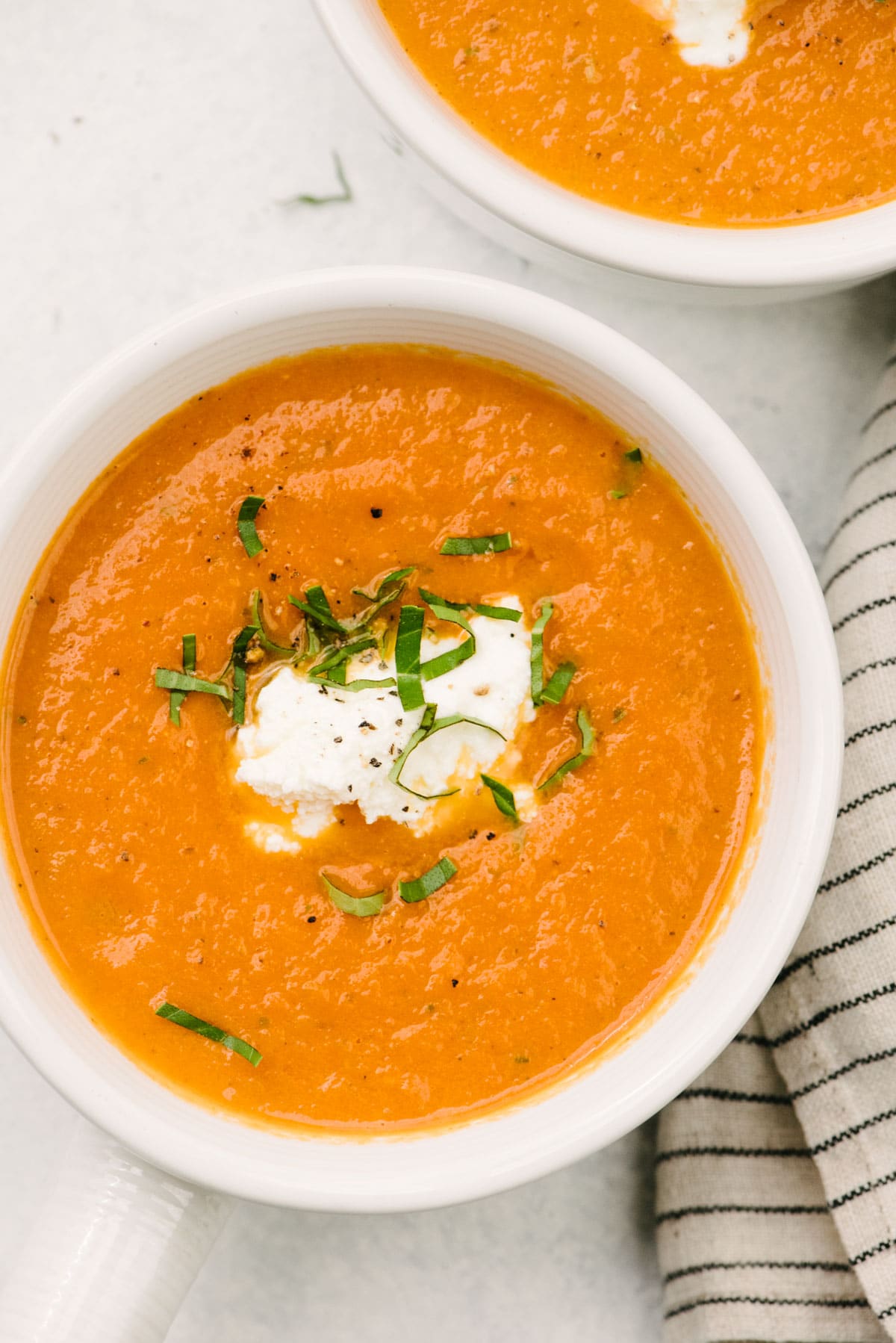 A bowl of creamy tomato basil soup made from fresh tomatoes, garnished with ricotta cheese and fresh basil.