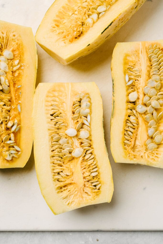 Delicata squash sliced in half on a cutting board, showing the seeds and pulp.