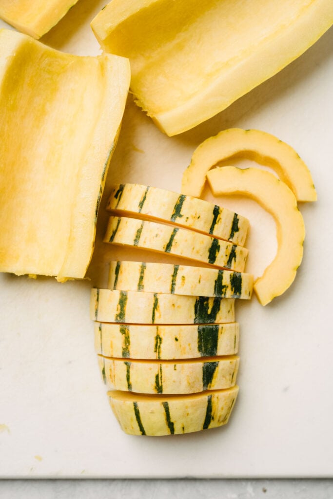 Delicata squash halves with the seeds and pulp removed, with one half sliced into half moons.
