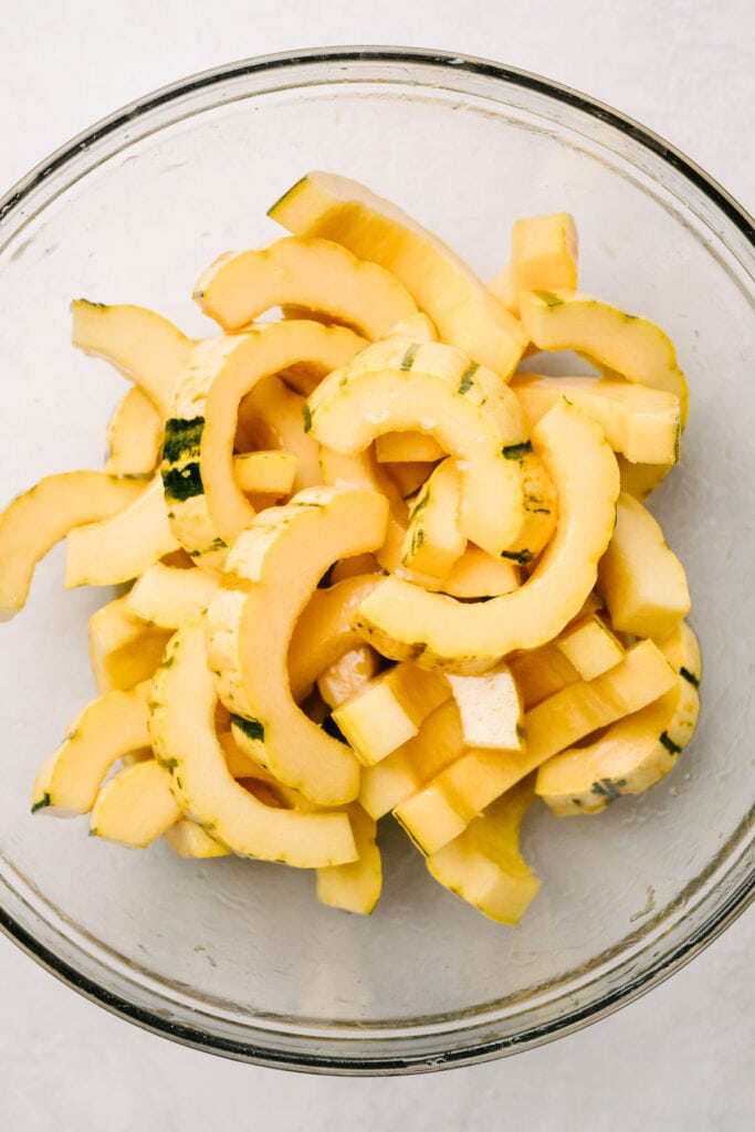Delicata squash slices tossed with maple butter in a large glass mixing bowl.