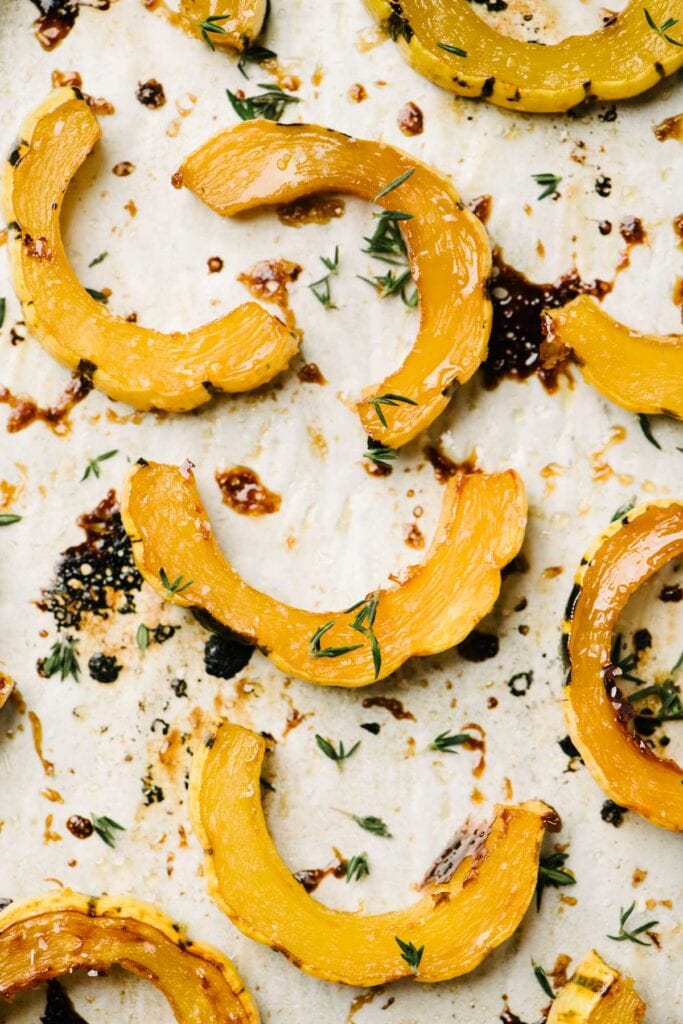 Close up view of roasted delicata squash slices garnished with fresh thyme on a parchment lined baking sheet.