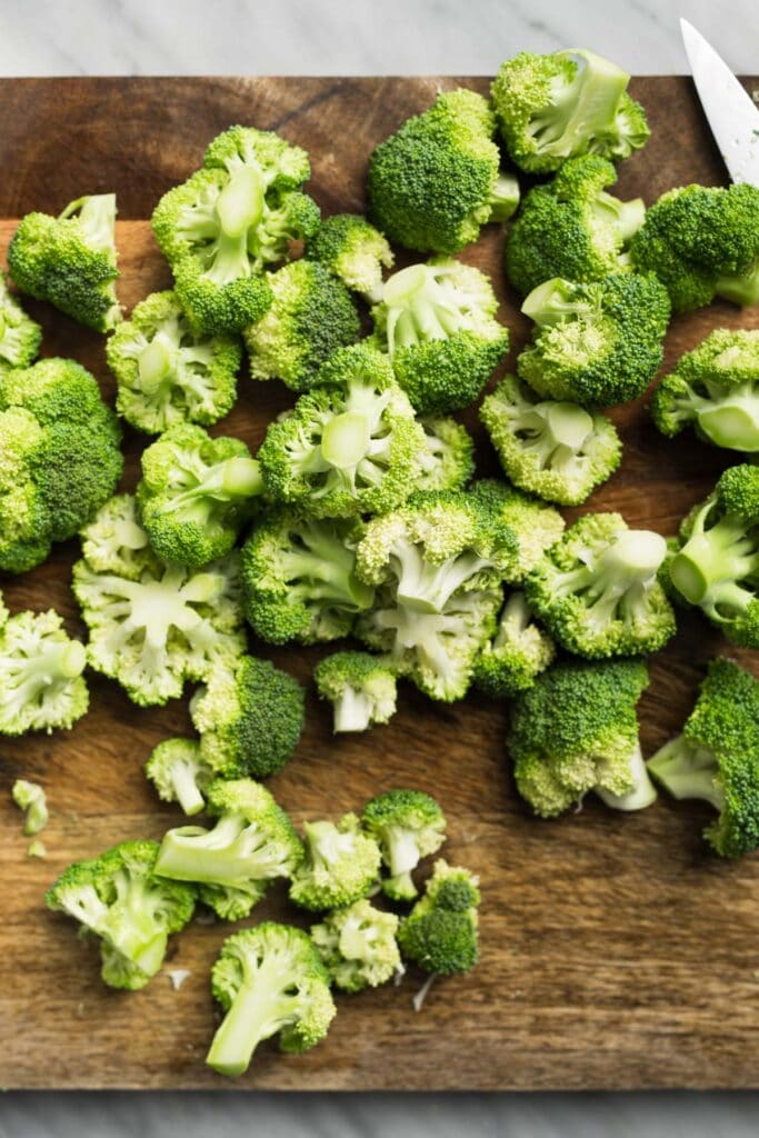 Broccoli florets scattered across a wood cutting board.