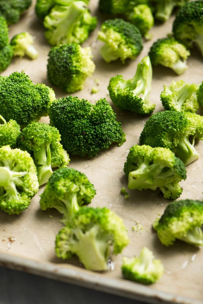 Broccoli florets tossed with olive oil, salt, and pepper on a parchment lined baking sheet.