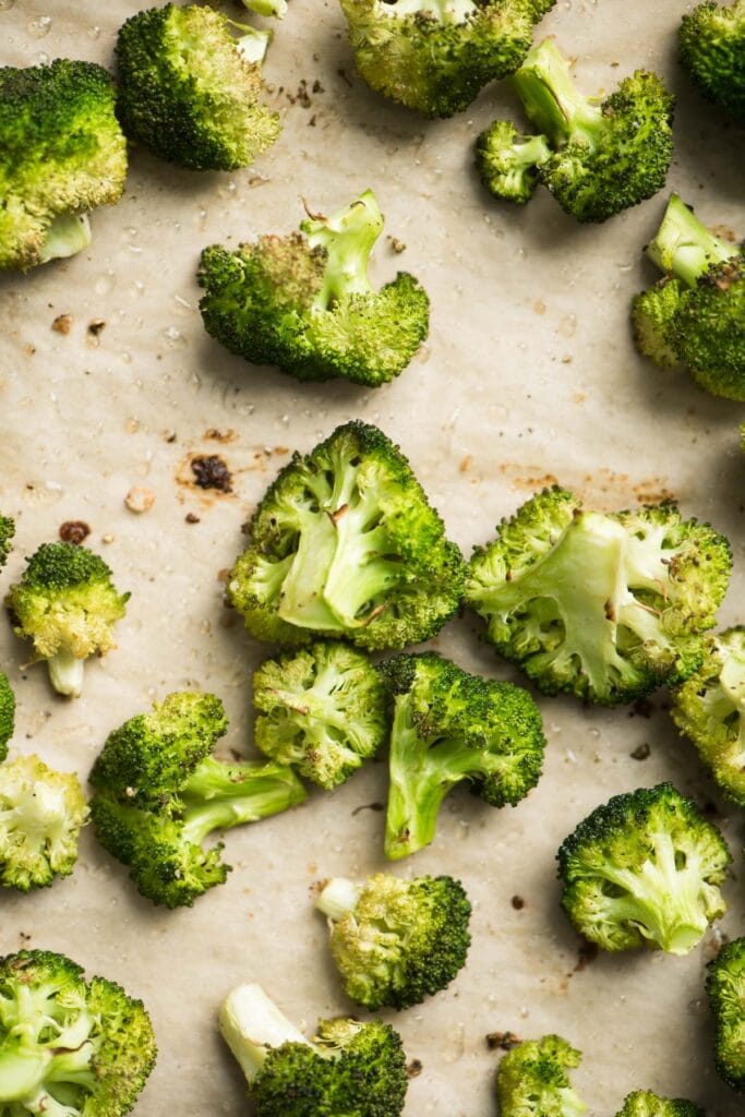 Roasted broccoli florets on a parchment lined baking sheet.