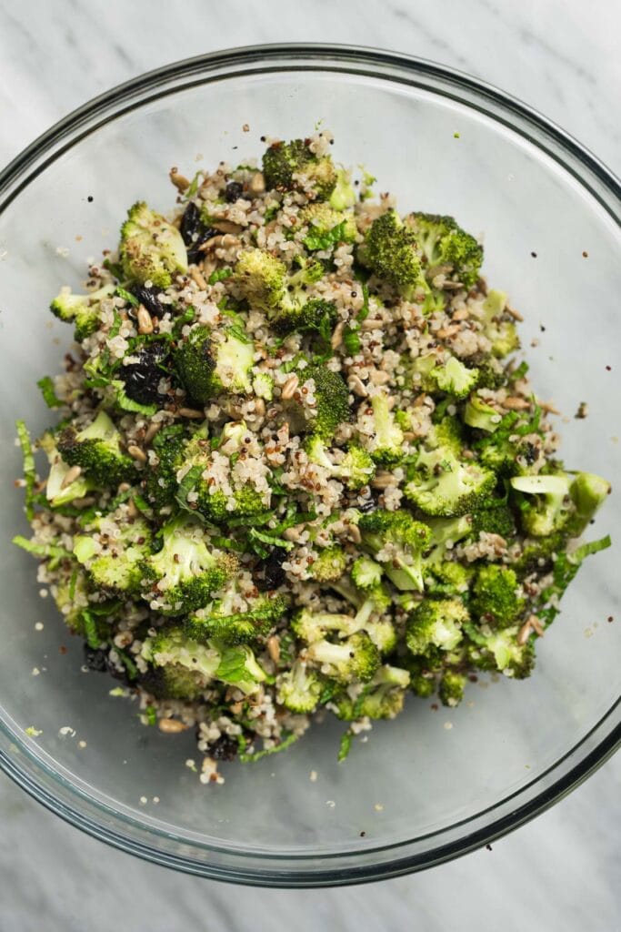Broccoli quinoa salad in a large glass bowl, made with roasted broccoli, quinoa, sunflower seeds, dried cherries, and fresh mint.