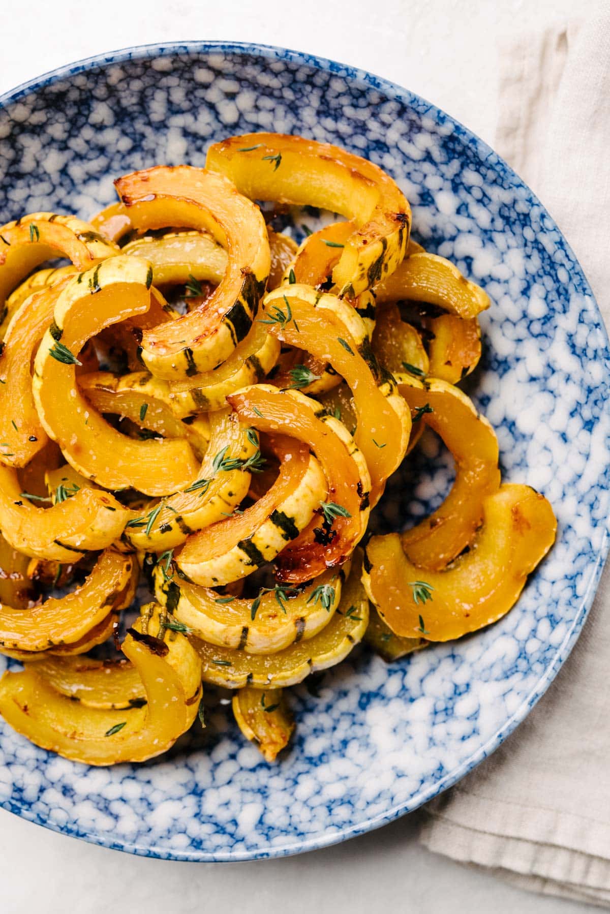 Roasted delicata squash slices in a blue speckled bowl, garnished with fresh thyme.