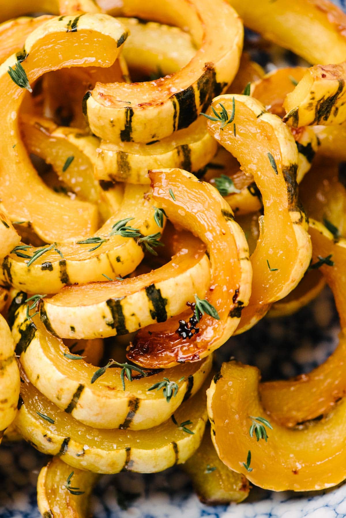 Side view, detail of roasted delicata squash slices in a blue speckled bowl, garnished with fresh thyme.