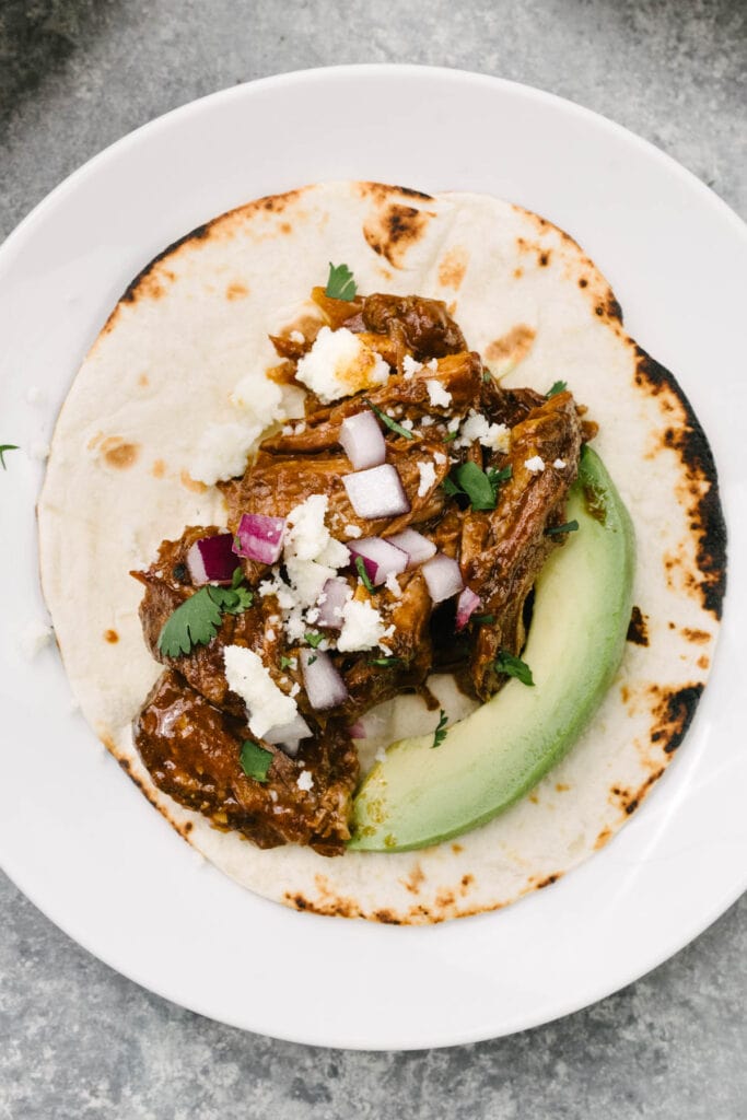 A soft flour tortilla layered with Mexican shredded beef, avocado, red onion, queso fresco, and cilantro.